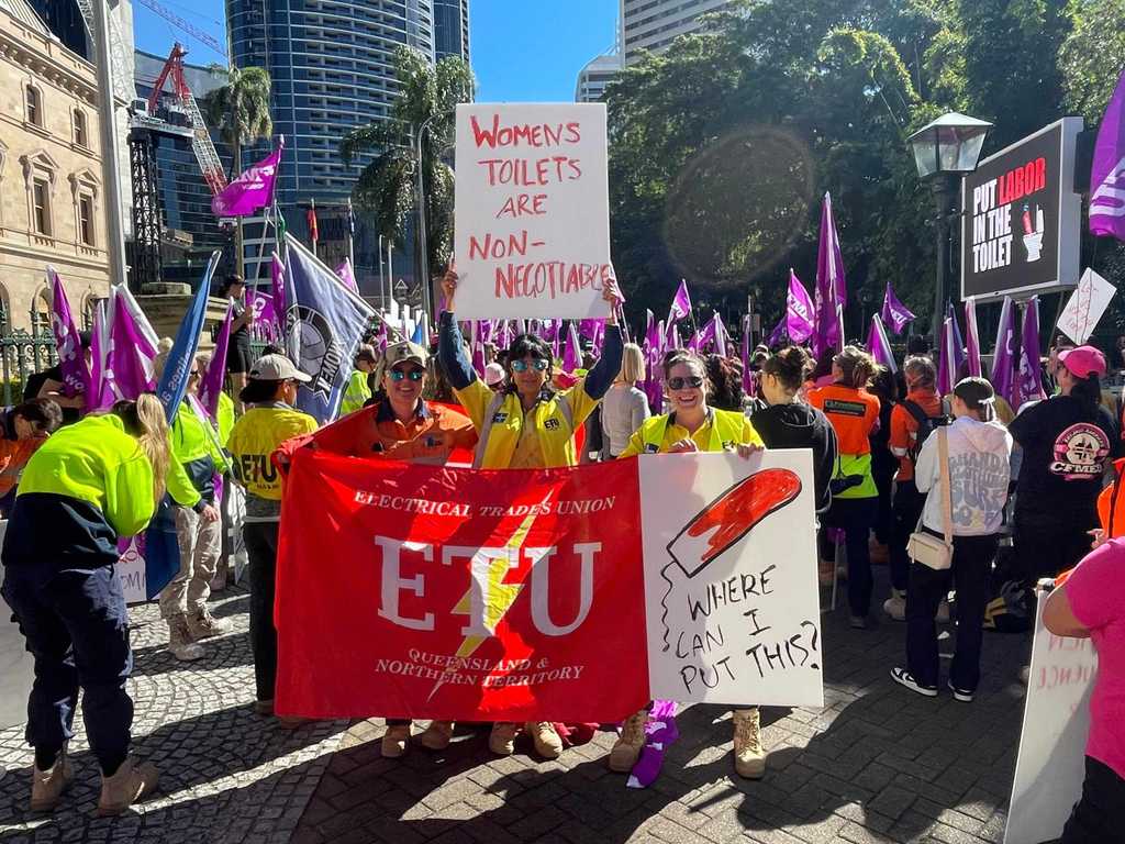 Women's Toilets Are Non-Negotiable A crowd of women construction workers holding signs and banners demanding better women's bathroom facilities. One sign reads "Women's Toilets Are Non-Negotiable," while another features a drawing of a tampon with the words "Where can I put this?" The protesters are wearing high-visibility work clothing, and numerous union flags and banners from the ETU and CFMEU are visible in the background.